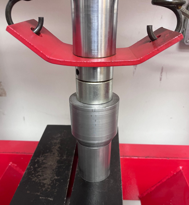 A photo showing a hydraulic press being used to expand a section of exhaust pipe using a custom-machined conical mandrel.