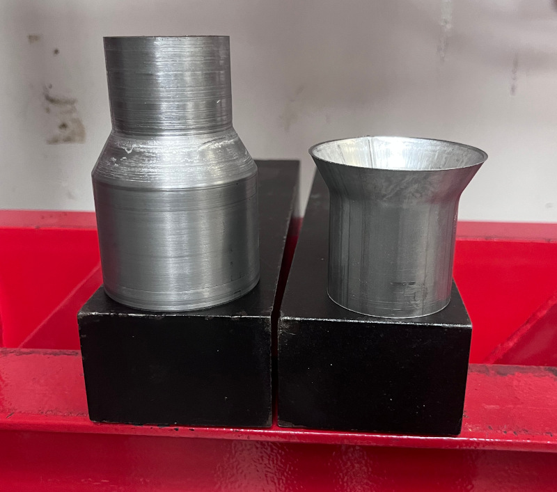 A photo showing a hydraulic press being used to expand a section of exhaust pipe using a custom-machined conical mandrel.