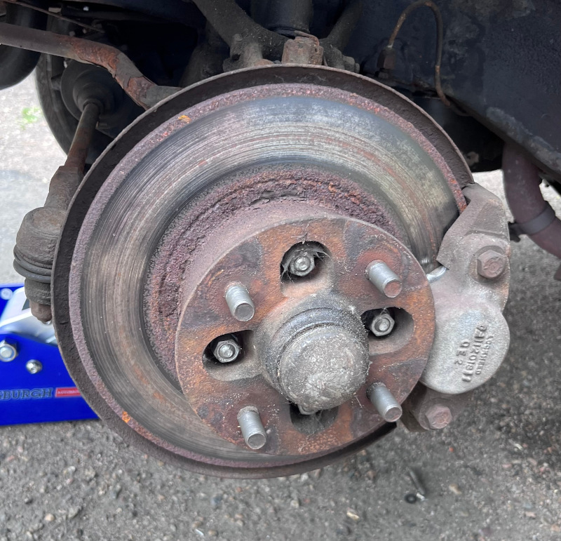 A photo of the front driver's side wheel hub, disc brake rotor, and brake caliper assembly as it appeared on the car prior to repair.