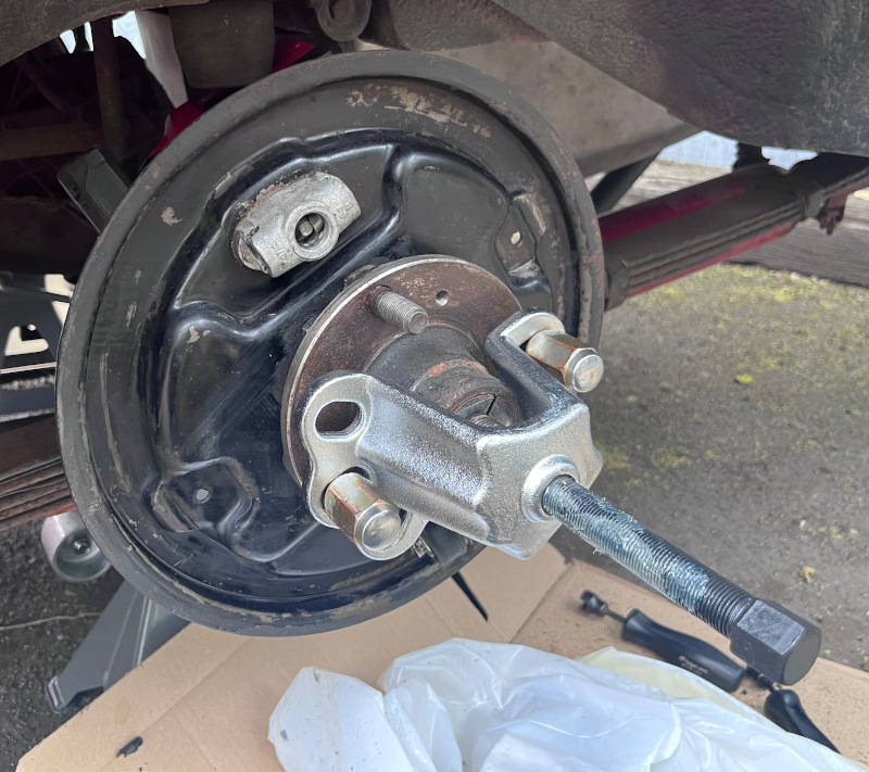 A photo showing the use of an axle hub puller to remove the driver's side rear axle hub from its axle.
